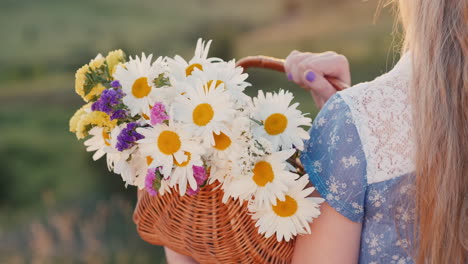 a child holds a basket of flowers stands in a meadows and green hills