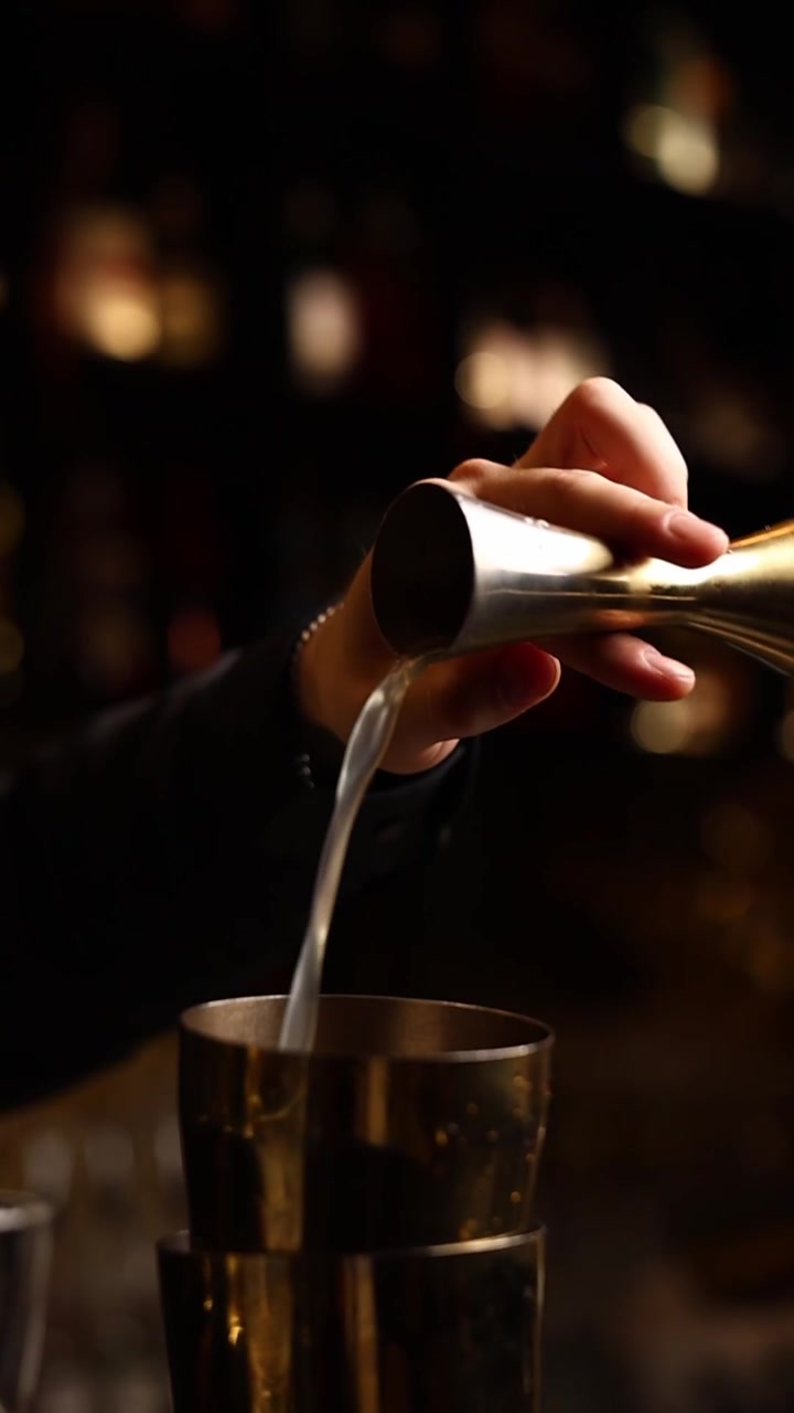Bartender hælder væske fra en jigger i en cocktailshaker