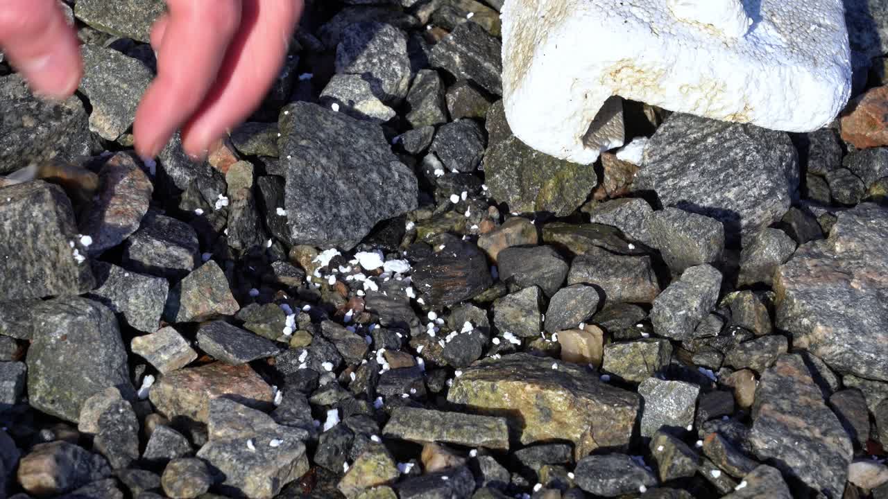 한 사람이 노르웨이의 바위투성이 해안선에서 작은 스티로폼 조각을 주우려고 합니다.