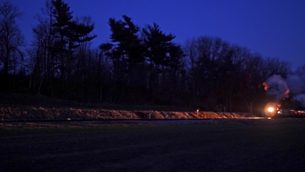 A Steam Passenger Train Blowing Smoke and Steam Traveling At Night
