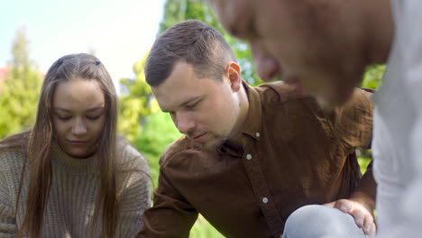 Close-up-view-of-a-group-of-men-and-women-friends-squatting-and-calculating-distance-between-petanque-balls-in-the-park