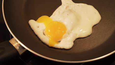 frying egg in a pan and piercing yolk with a fork