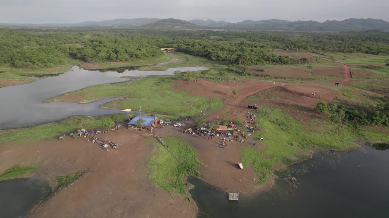 드론이 찍은 풀 아웃 숏에서 넓은 강가, 텐트, 차량이 있는 활기찬 캠프가 드러나 외딴 곳의 자연과 모험적인 라이프스타일을 강조해요