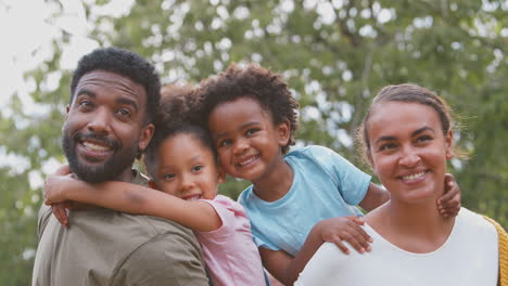 portrait of  family outdoors in garden with parents giving children piggybacks