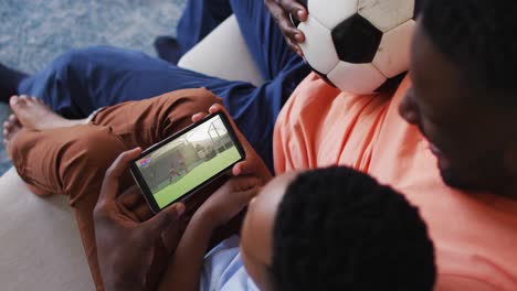 Composite-of-father-and-son-at-home-watching-hockey-match-on-smartphone