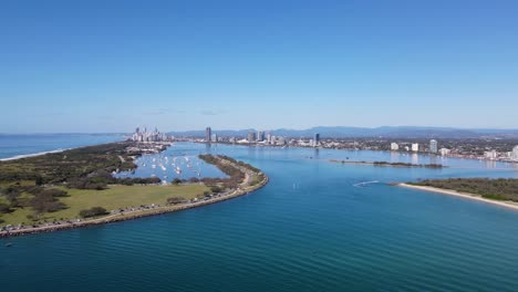 High-static-drone-view-of-a-large-bay-and-boat-harbor-protected-from-the-ocean-with-an-urban-skyline-and-mountain-range-in-the-distance