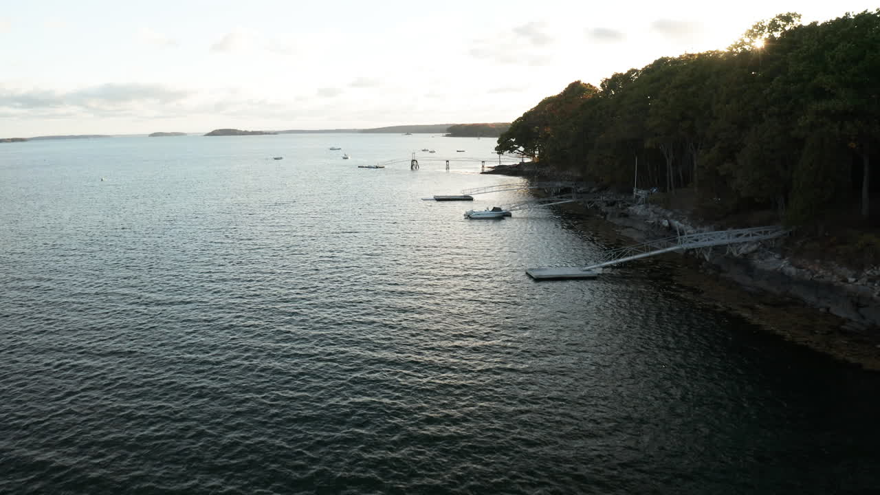 съемка с беспилотника с высоты полета над прибрежными доками штата мэн с лучами солнца, проглядывающими сквозь деревья