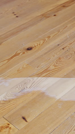 close-up vertical shot of electric drum sander in operation on pine wood floor, showing clear sanding marks and the transition from unsanded to sanded wood, power cord connected, machine detail