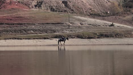 Person,-Die-Auf-Einem-Pferd-Am-Strand-Eines-Sees-Reitet