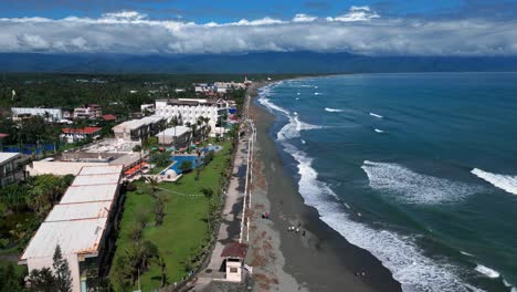 a wide drone shot captures the ocean waves crashing against the shore, where resort houses are neatly lined up along the coastline.