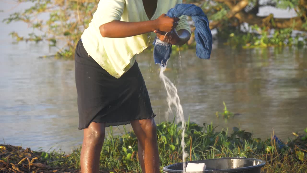 Slow motion close up of African woman wringing water from clothes she is washing on the shores of Lake Victoria in the early morning sun.