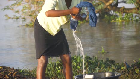 slow motion close up of african woman wringing water from clothes she is washing on the shores of lake victoria in the early morning sun.