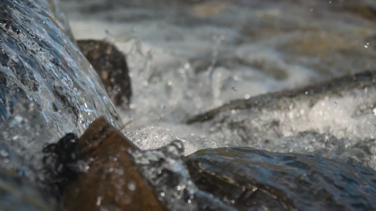 Primo piano di una cascata cristallina che schizza sulle rocce in un ruscello al rallentatore
