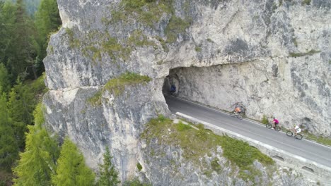 aerial of an male cyclist entering tunnel on italian dolomites while other cyclists are catching up