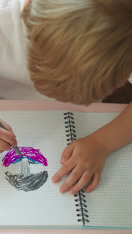 toddler boy draws while sister pins tags in eraser and takes ribbon rolls at small desk in classroom upper view. little children do art tasks at home