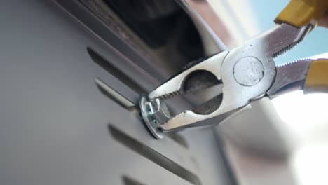 close up view mechanician use pliers tighten a bolt of the car's license plate on the car