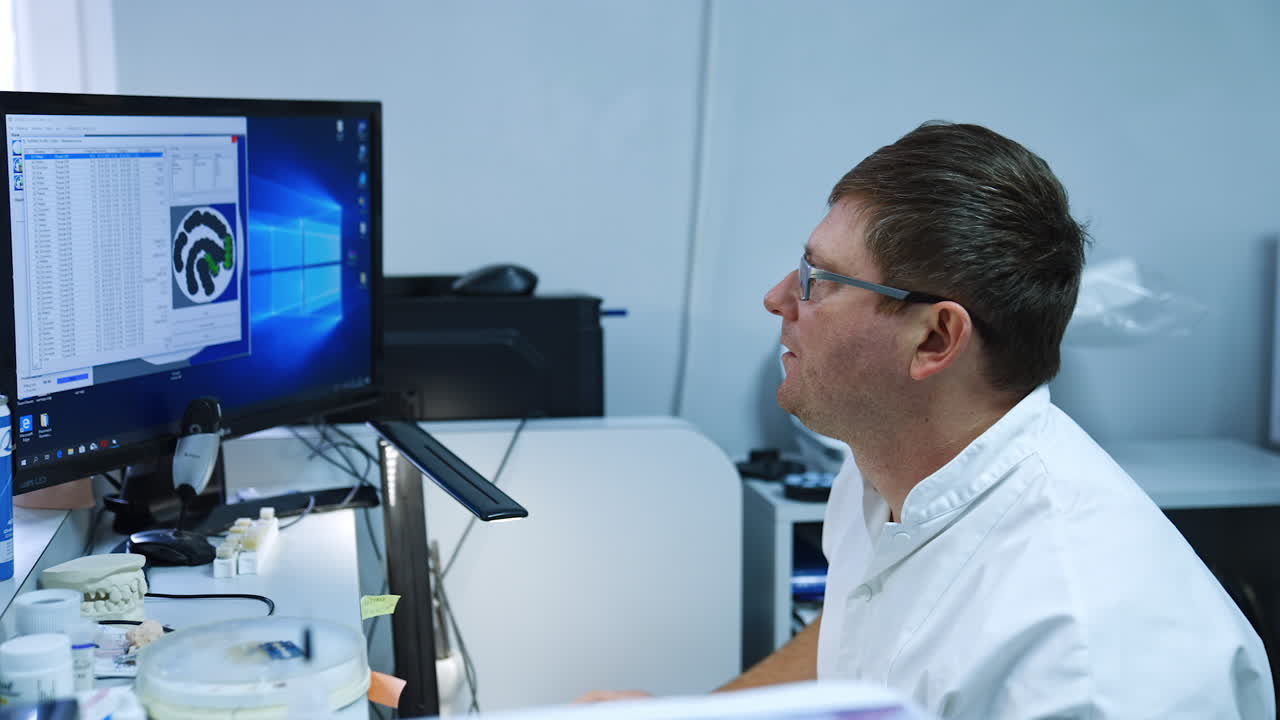 Male lab technician sits looking intently at computer screen. Orthodontic care in hospital.