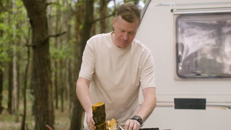 caucasian man putting wood in a grill at the camping in the forest