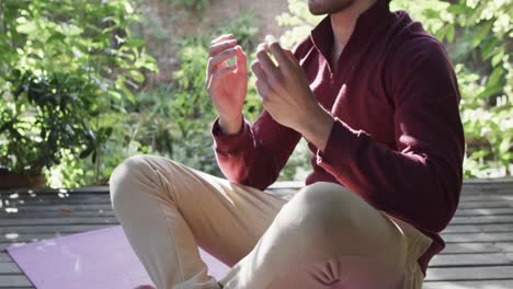 sección media de un hombre caucásico practicando meditación de yoga en la terraza en la naturaleza soleada, cámara lenta