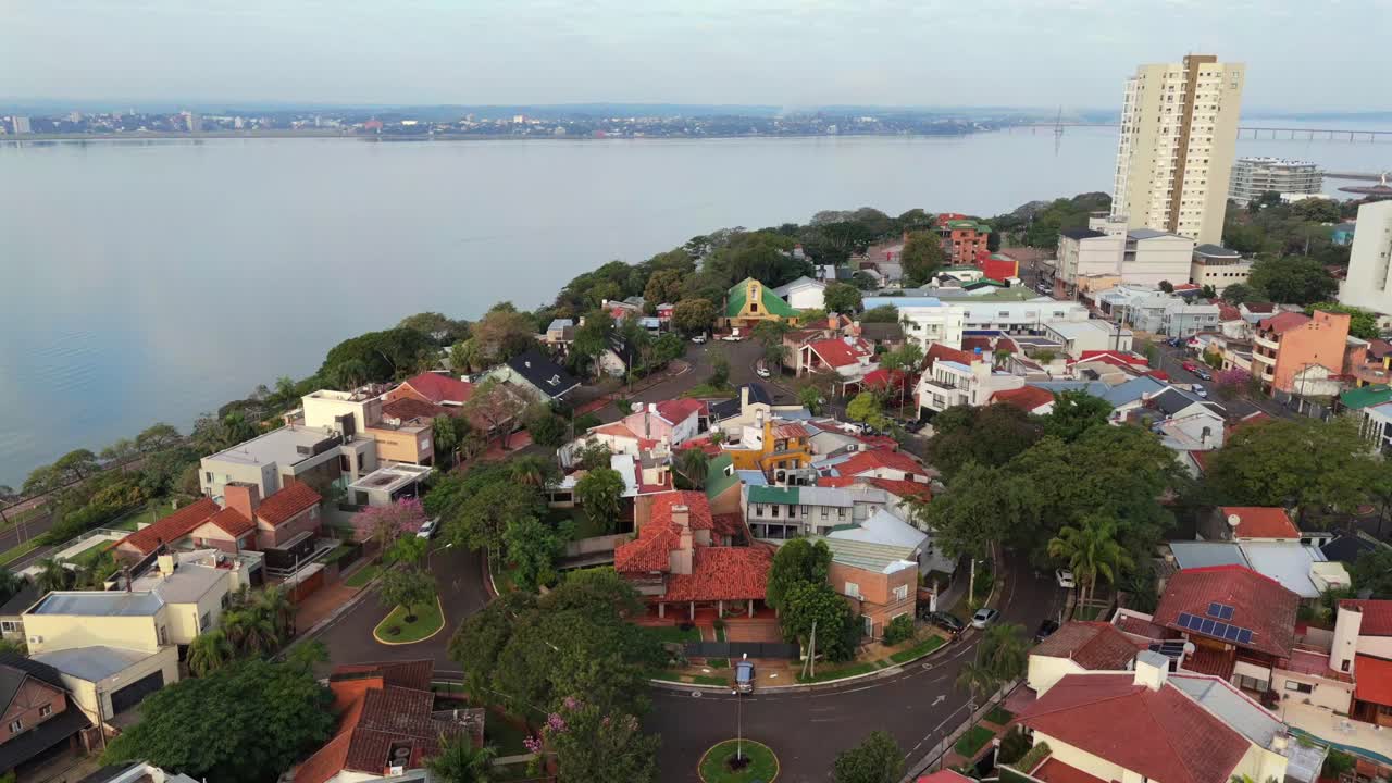 Video di drone in orbita sopra le case residenziali mediterranee a Posadas, Argentina, con fiume calmo e skyline della città all'orizzonte durante il pomeriggio