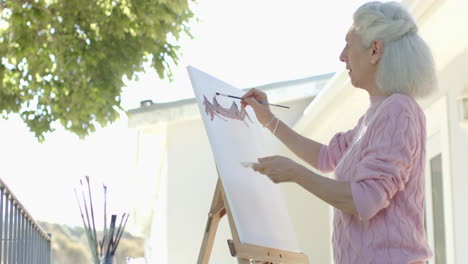 happy senior biracial woman painting at balcony at home, slow motion