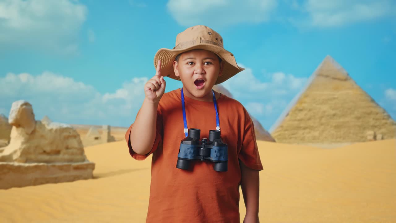 Asian Boy With A Hat And Binoculars Thinking And Looking Around Then Raising His Index Finger While Traveling In Giza Pyramid. Boy Researcher, Travel Tourism Adventure Concept