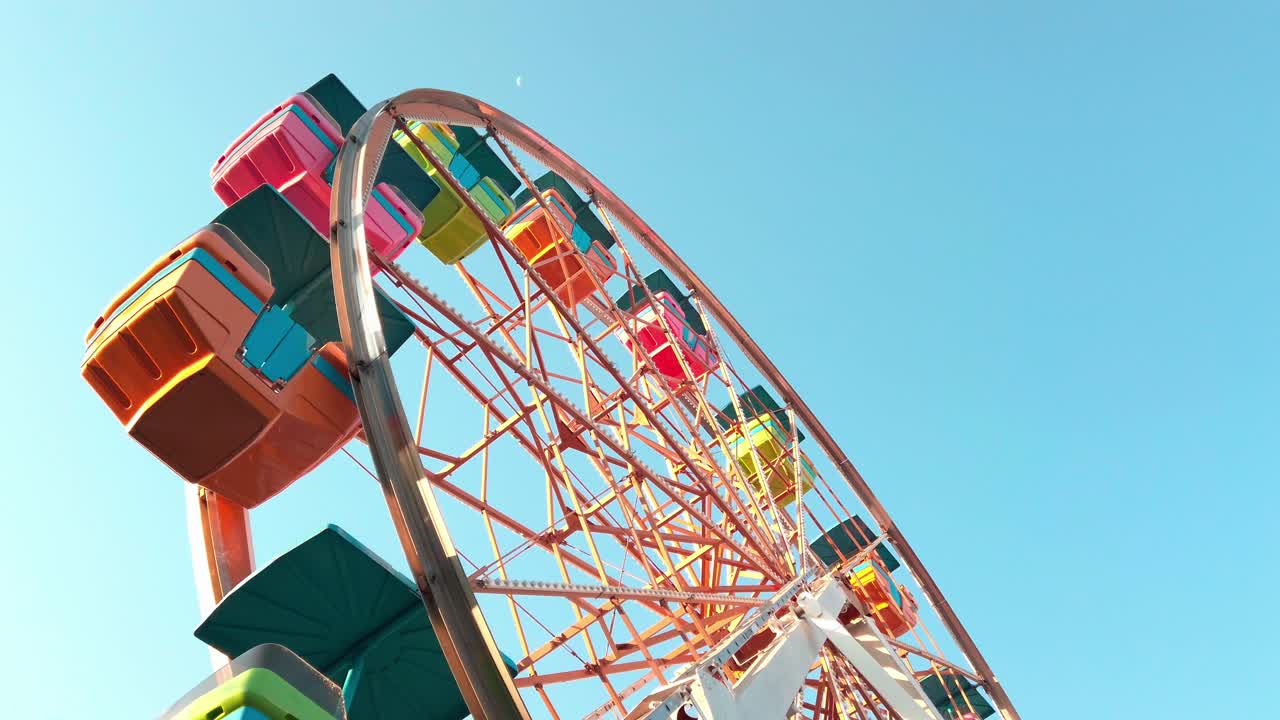 Colorful ferris wheel turning under clear blue sky in Boneless plaza, daytime joy ride