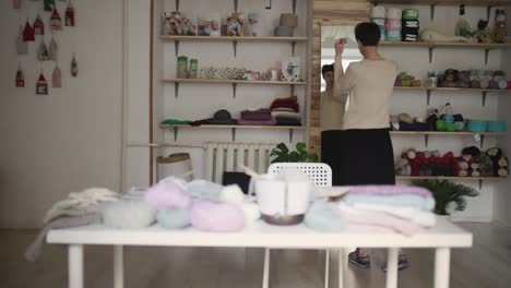 young woman looking in mirror in textile workshop. hipster woman trying sweater