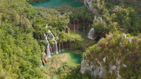 Incredible-aerial-drone-view-of-bright-turquoise-lakes-connected-with-waterfalls-between-rocky-cliffs-and-dense-forest