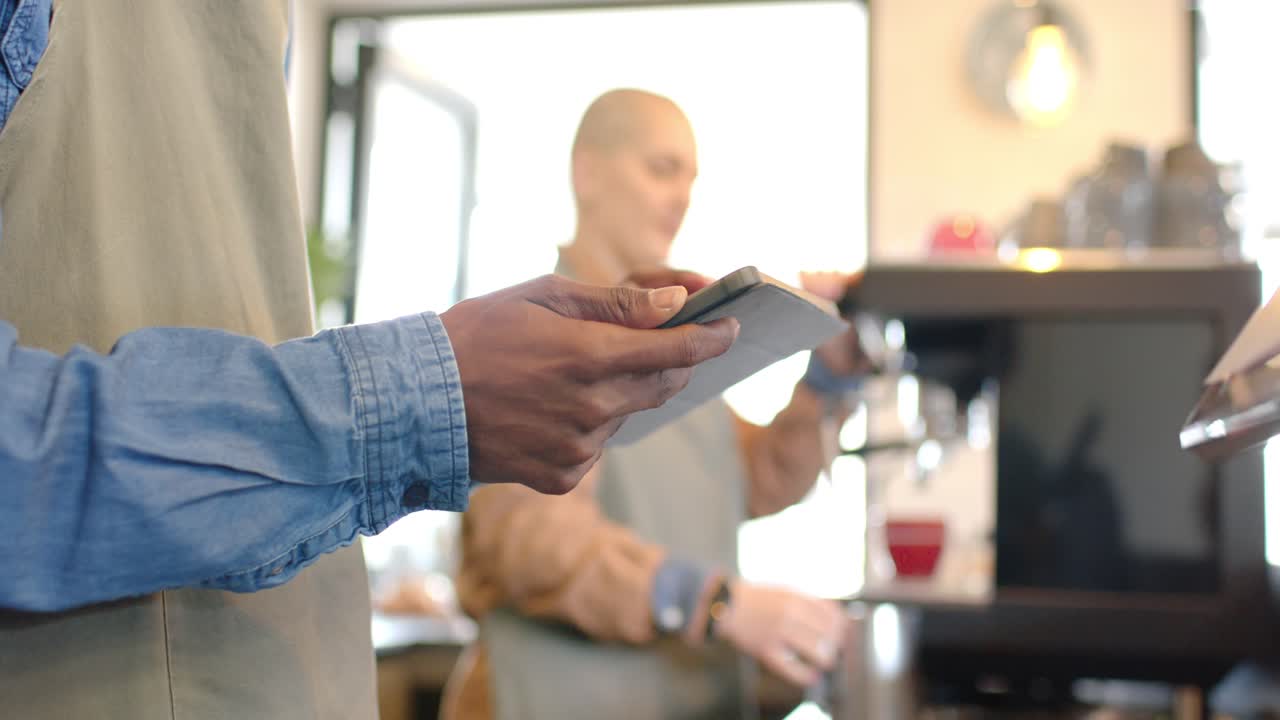 Diverse coworkers tapping tablet viewing order, tamping portafilter and steaming pitcher at counter