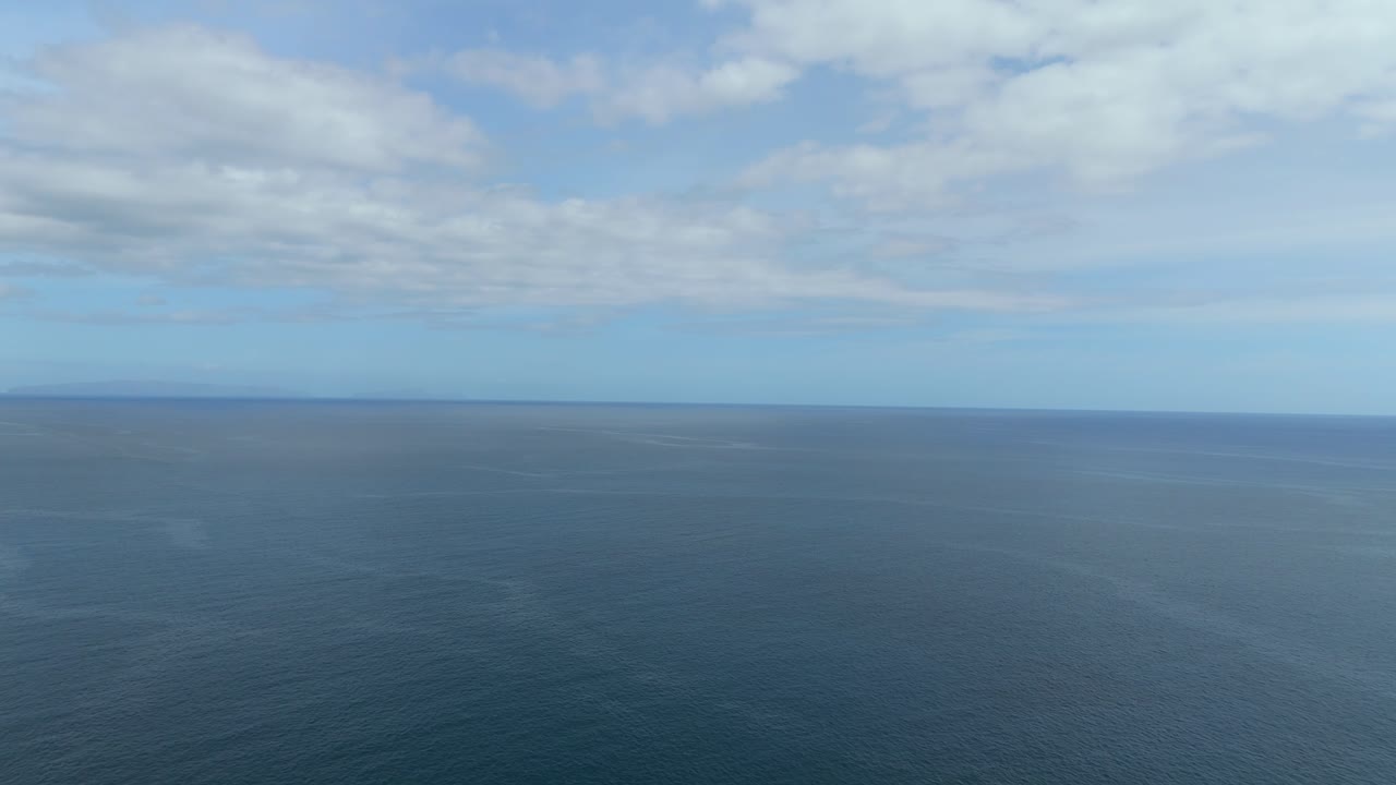 Wide aerial shot of ocean and horizon with soft cloud formations in a bright blue sky, ideal for visual overlays, b-roll backgrounds or motion graphics templates.