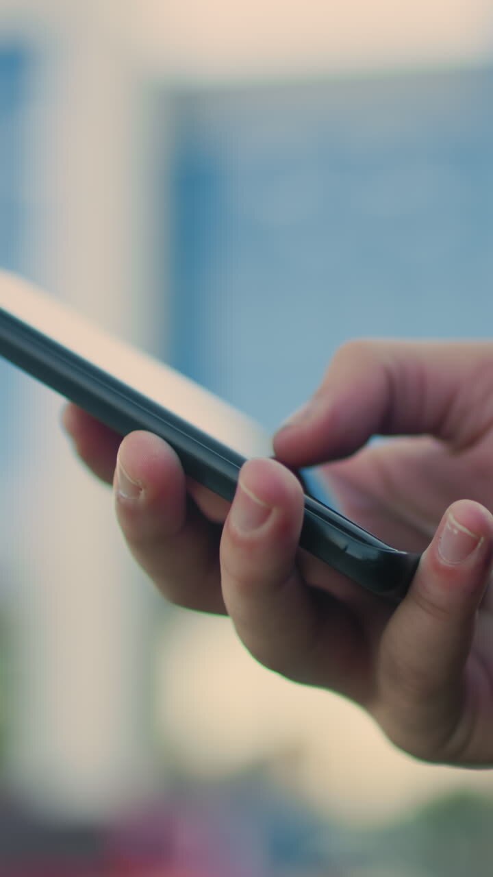 Close up of hand operating smartphone in modern urban environment with blurred background featuring contemporary glass building and greenery