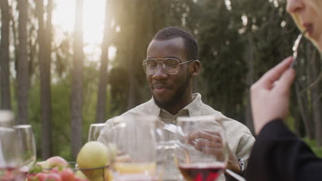 middle aged man eating and talking to his friends sitting at table during an outdoor party in the park 1