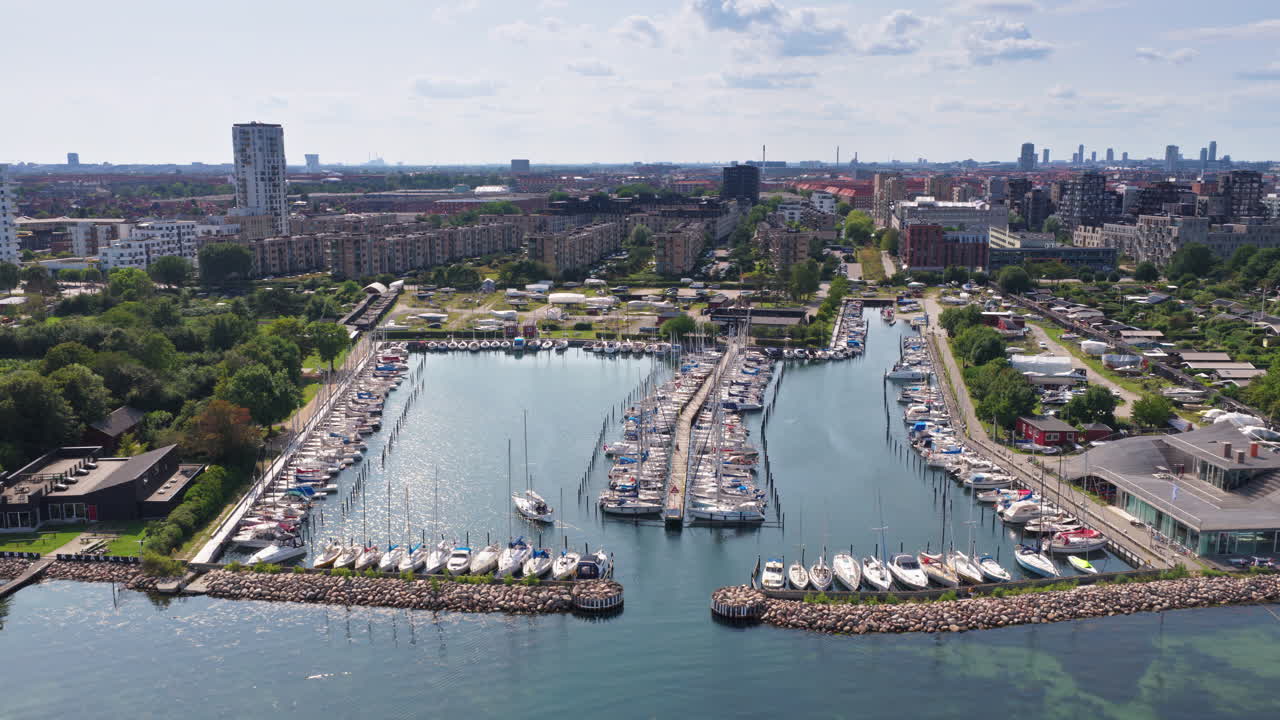 Aerial drone view of the marina filled with sailboats, surrounded by residential blocks and the green coast in Copenhagen, Denmark