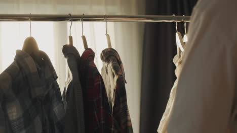 a man chooses his clothes near a rack with a coat hanger, from behind he is illuminated by the sun's rays from the window. rear view