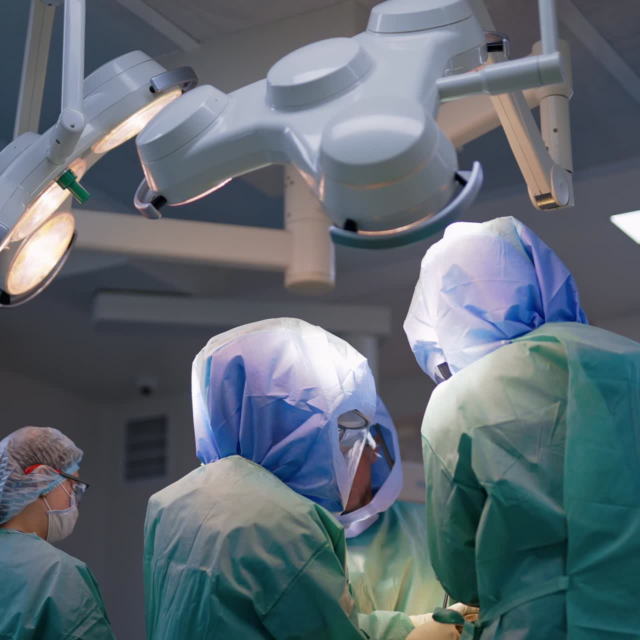Rear view of a surgeons wearing protective suits and helmets. Team of doctors stand around the surgery table