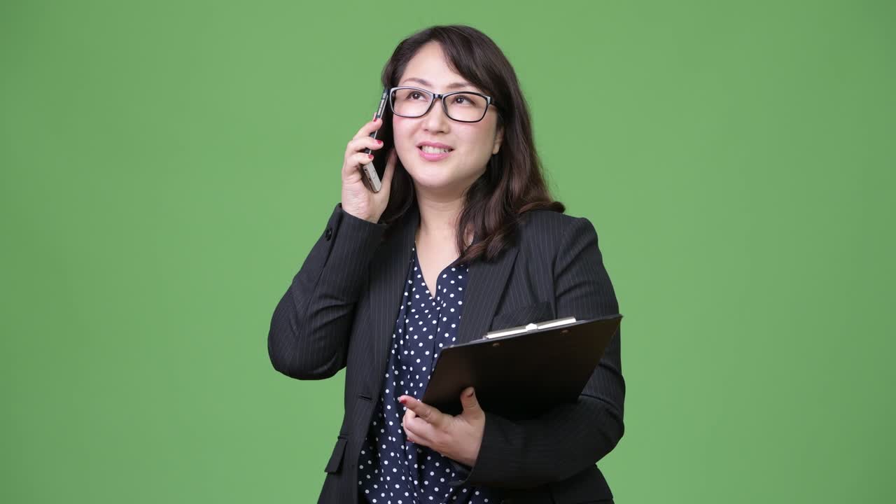 Zralá krásná asijská podnikatelka používající telefon a držící desky na dokumenty