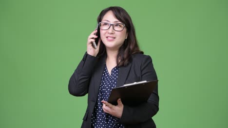 una hermosa mujer de negocios asiática madura usando el teléfono mientras sostiene el portapapeles