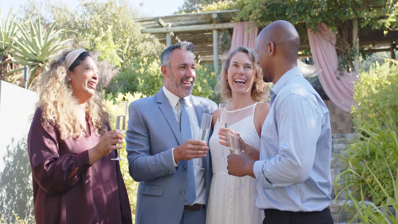 Diverse couple with two guests, woman in plum dress raising flute, others clinking, toasting garden