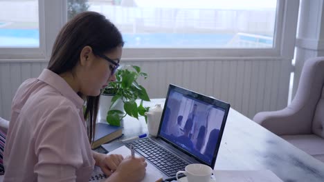 e-learning, young female spectacled passes online teaching for self-development uses laptop computer and makes notes in notebook