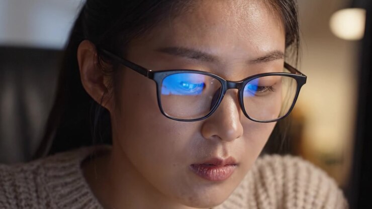 Concentrata sul lavoro: primo piano di una giovane donna con gli occhiali, assorta nei pensieri mentre lavora al computer durante una sessione notturna