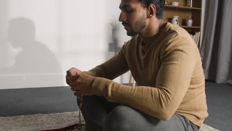 close up of muslim man praying holding prayer beads casting shadow on wall behind 2