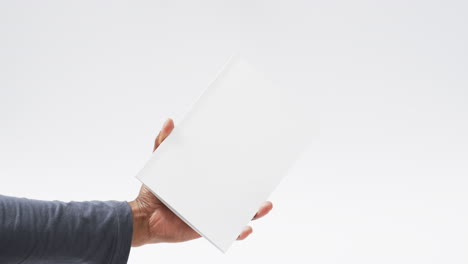 Video-of-hand-of-african-american-man-holding-book-with-blank-pages,-copy-space-on-white-background