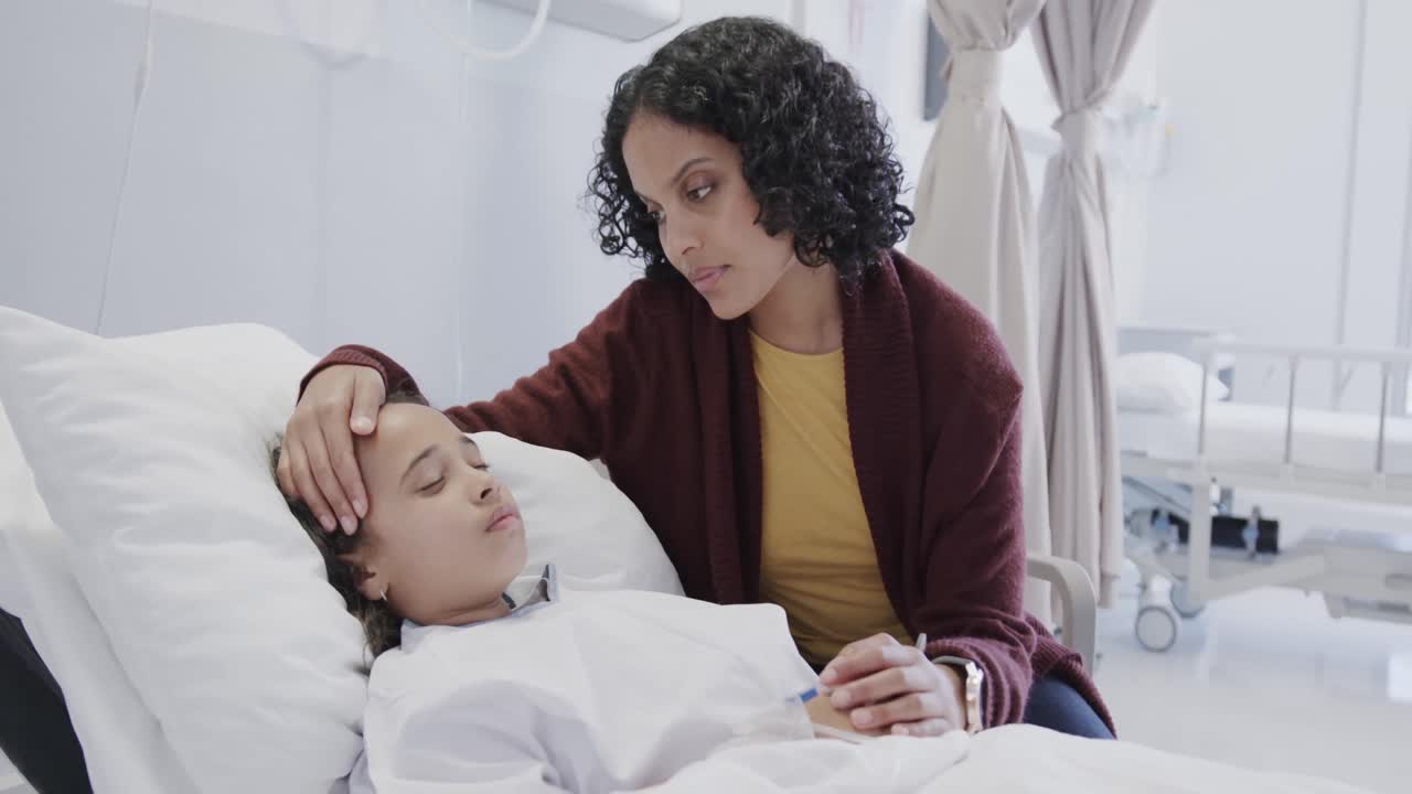 Worried biracial mother stroking her sleeping sick daughter patient in hospital in slow motion
