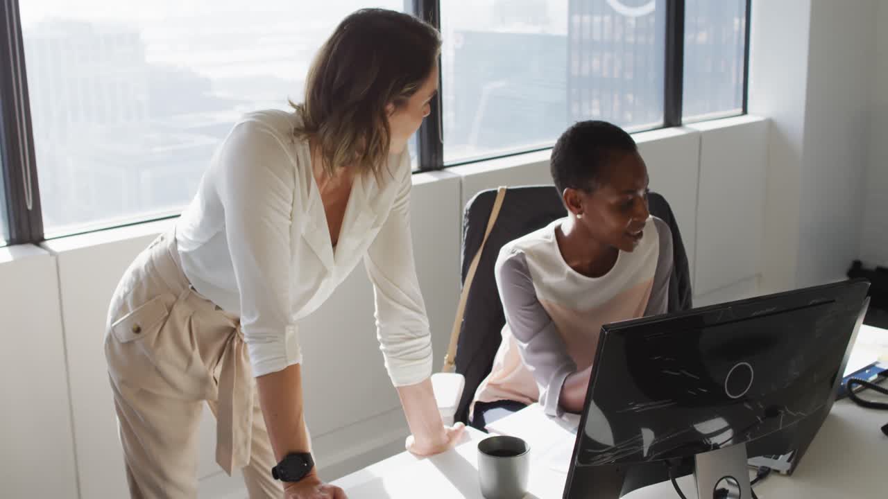 Two diverse female colleagues looking at laptop and discussing in office