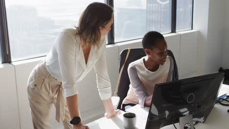 dos colegas femeninas diversas mirando la computadora portátil y discutiendo en la oficina