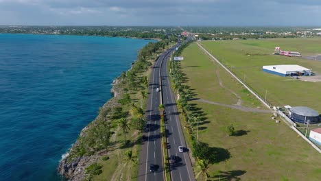 Aerial-flyover-coastal-road-with-driving-cars-near-airport-of-Santo-Domingo-during-sunny-day