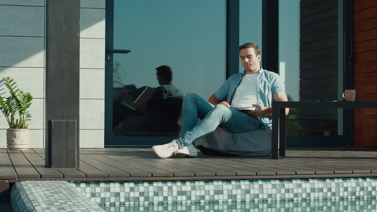 피곤한 남자가 럭셔리 하우스 테라스에서 노트북을 닫고, 예쁜 프리랜서가 가방 의자에서 휴식을 취하고.