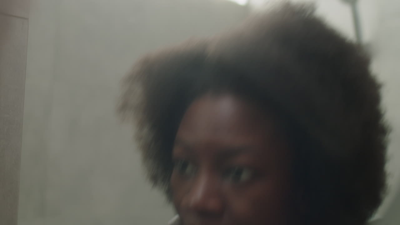 Donna di colore che si lava il viso e si guarda allo specchio del bagno