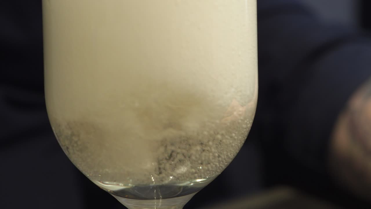 Vertido espumoso de vino espumoso en una copa estrecha - Primer plano